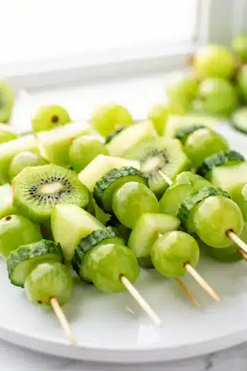 Green Fruit Kabobs 11 Colorful green fruit kabobs with kiwi and honeydew on wooden skewers.