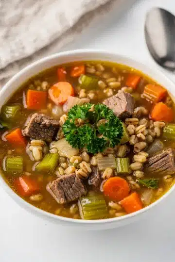 Slow Cooker Beef Barley Soup 13 Slow cooker beef barley soup with tender beef chunks and sliced carrots in rustic bowl.