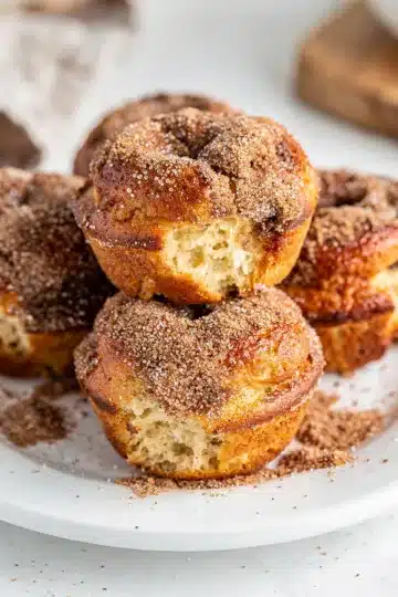 Cinnamon Sugar Donut Muffins 11 Cinnamon sugar donut muffins on a white plate with cinnamon sticks.