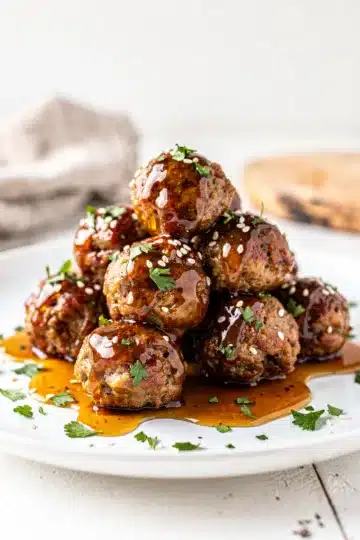 Honey Garlic Meatballs 12 Honey garlic meatballs in a glossy sticky sauce on a white plate