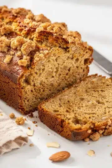 Banana Bread 11 Moist banana bread slice with cinnamon almond crumble topping on rustic board.