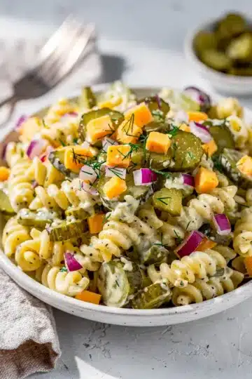 Creamy Dill Pickle Pasta Salad 12 Creamy dill pickle pasta salad in a white bowl with fresh ingredients.