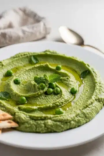 Spring Pea and Mint Hummus 11 Creamy spring pea and mint hummus garnished with peas and olive oil.