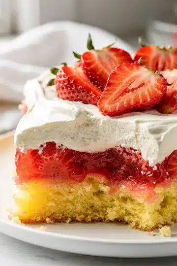 Old Fashioned Strawberry Jello Poke Cake 11 Old Fashioned strawberry jello poke cake slice with whipped cream and fresh strawberries.