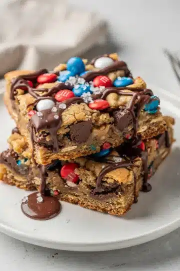 Fourth of July Monster Cookie Bars 14 Fourth of July monster cookie bars with M&M's and chocolate chips on a wooden table.