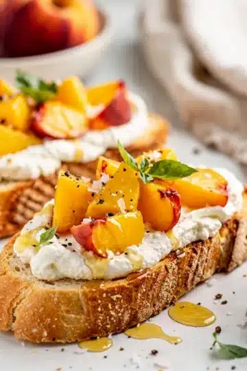 Peach Bruschetta with Whipped Ricotta 12 Rustic peach bruschetta with whipped ricotta on a dark slate board.