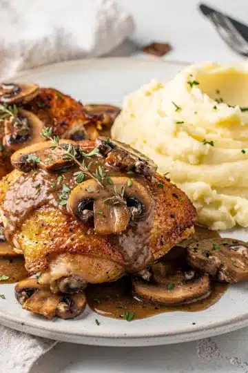 Smothered Chicken Thighs with Mushroom Gravy 12 Crispy smothered chicken thighs in creamy mushroom gravy on rustic plate.