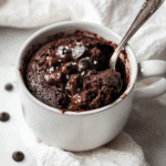 Gooey chocolate protein mug cake topped with melted chocolate chips and sea salt in a white ceramic mug