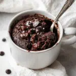 Gooey chocolate protein mug cake topped with melted chocolate chips and sea salt in a white ceramic mug