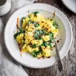 Scrambled eggs with spinach in a white bowl with avocado and hot sauce