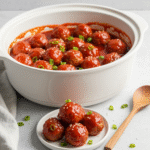 Sweet Chili Meatballs Crockpot 6 Sweet chili meatballs in a white crockpot with garnish.