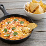Creamy baked elote dip with cotija cheese and tortilla chips.