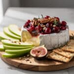 Warm baked brie cheese topped with cranberry sauce and toasted pecans appetizer.