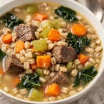 Hearty beef and barley soup with vegetables in a rustic bowl on wood.
