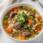 Hearty beef and barley soup in a rustic bowl with vegetables and parsley.