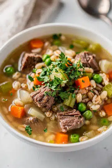 Hearty beef and barley soup in a rustic bowl with vegetables and parsley.