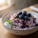 High protein blueberry cheesecake oats in a creamy layered glass jar.