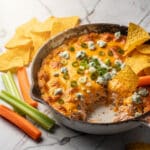 Golden bubbly Buffalo chicken dip with melted cheese and fresh vegetables.