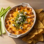 Spicy buffalo chicken dip with melted cheese served with chips and celery.