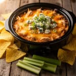 Creamy buffalo chicken dip in a crock pot with chips and celery