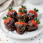 Chocolate covered strawberries with colorful sprinkles on a marble surface.