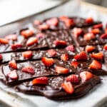 Chocolate covered strawberry bark with fresh red strawberries on white marble.