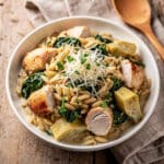 Creamy orzo pasta with chicken spinach and artichokes in a bowl.