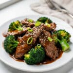 Crockpot beef and broccoli with glossy sauce over rice in ceramic bowl.