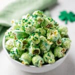 Vibrant green sprinkle popcorn recipe in a clear glass bowl on wood.