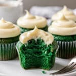 Green velvet cupcakes with cream cheese frosting on a rustic wooden board.
