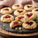 Homemade heart jam thumbprint cookies with vibrant red filling on rustic board