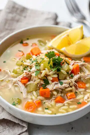Lemon chicken orzo soup in a bowl with carrots, celery, and fresh parsley.