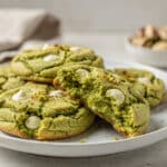 Soft green pistachio pudding cookies with white chocolate chips on a white plate.