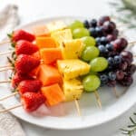 Colorful rainbow fruit skewers with yogurt dip on a rustic wooden board.