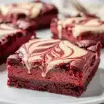 Red velvet cheesecake bars with dramatic marbled swirl on marble slab.