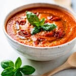 Creamy roasted tomato basil soup recipe in a rustic kitchen setting.