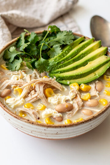 Creamy slow cooker white chicken chili in a white ceramic bowl with cilantro garnish.