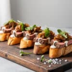 Steak crostini with horseradish sauce and caramelized onions on a wooden board.