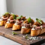 Steak crostini with horseradish sauce and caramelized onions on a wooden board.