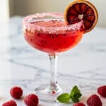 Vibrant pink Valentine's mocktail with raspberries and a salted rim.
