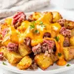 Cheesy corned beef hash with crispy potatoes and sunny side up eggs in cast iron skillet.