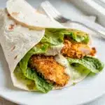 Crispy chicken Caesar wrap with golden strips and creamy glossy dressing.