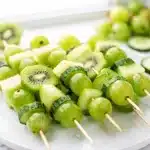Colorful green fruit kabobs with kiwi and honeydew on wooden skewers.