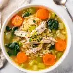 Creamy lemon chicken orzo soup with carrots and spinach in rustic bowl