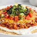 Layered taco dip with beans cheese salsa lettuce tomatoes olives and chips