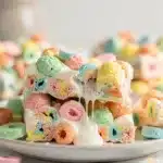 Gooey Lucky Charms marshmallow cereal bars with colorful pieces on white plate
