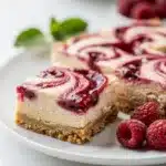 Creamy raspberry cheesecake bars with a vibrant jam swirl on graham crust