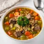 Slow cooker beef barley soup with tender beef chunks and sliced carrots in rustic bowl.