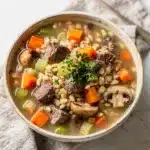 Hearty slow cooker beef barley soup with tender meat and vegetables in broth.