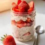 Creamy strawberry protein overnight oats in a clear glass jar with toppings.